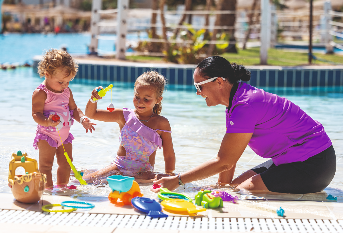 A photo taken at Holiday Village Red Sea with a member of staff playing with two small children beside the pool.