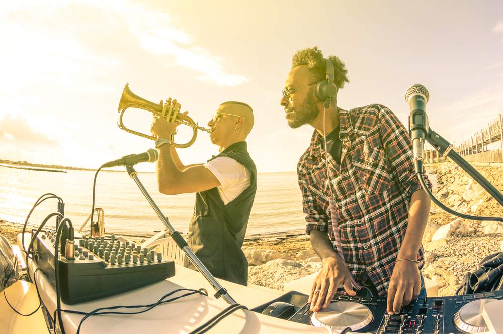 Dj playing summer hits at sunset beach party with trumpet jazz performer