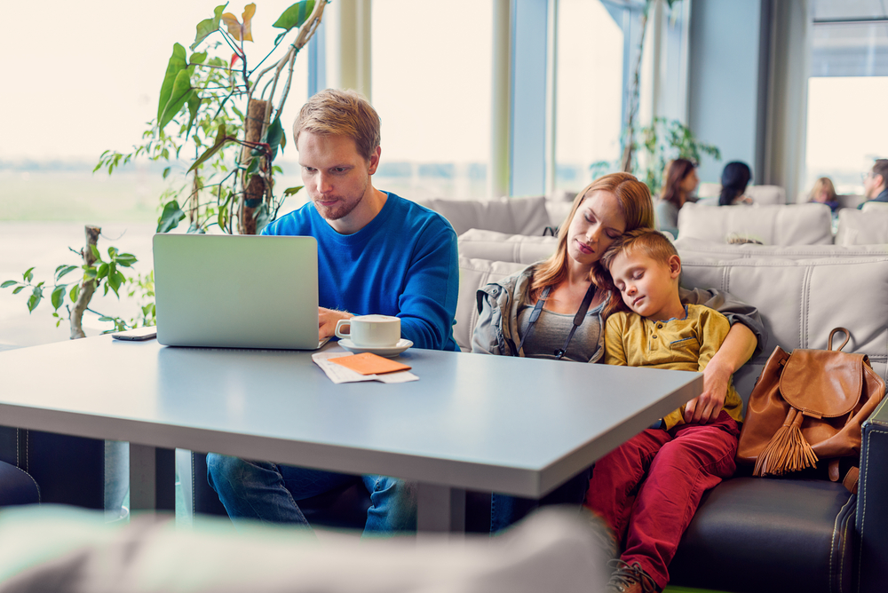 young father enjoying laptop while mother and son sleeping on couch in airport lounge