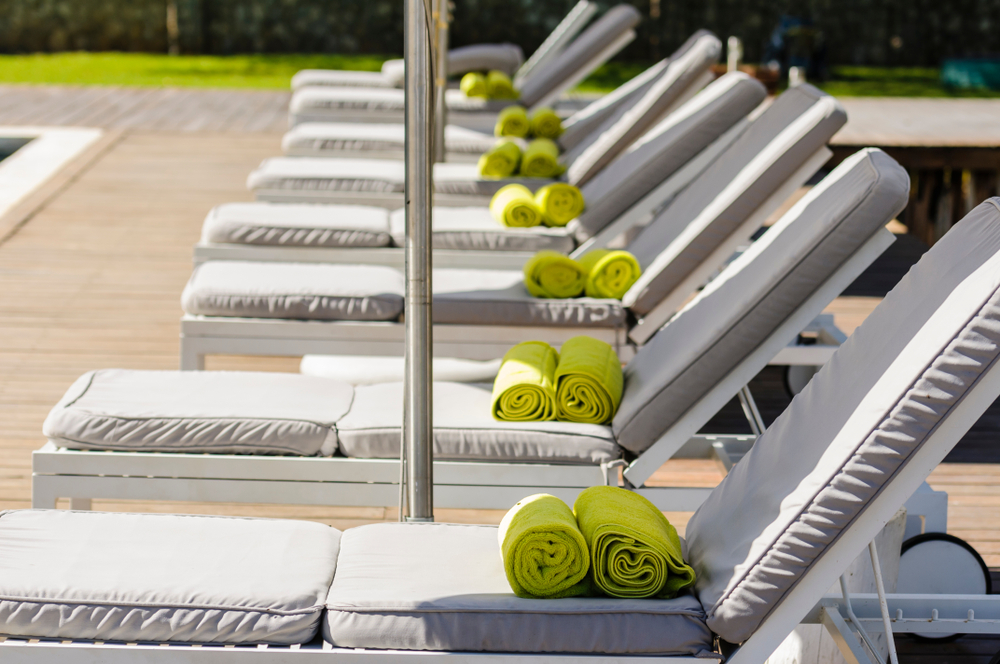 Green towels on a row of empty sunloungers beside a swimming pool