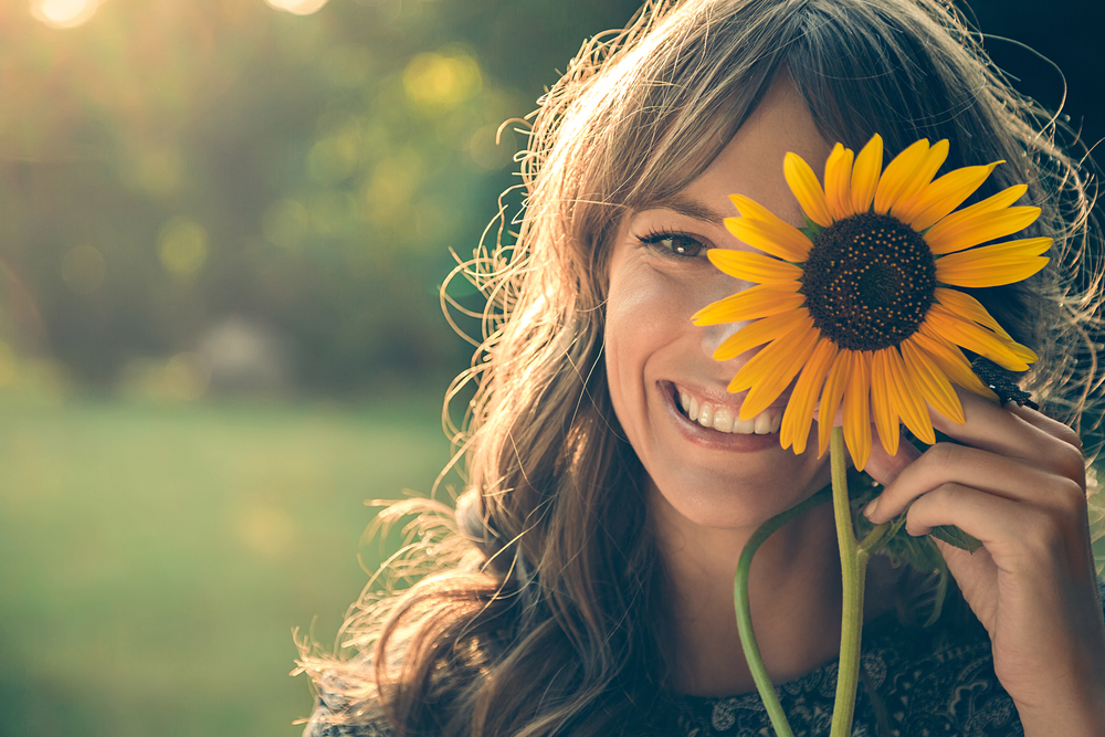 Girl hiding half of face behind sunflower whilst smiling