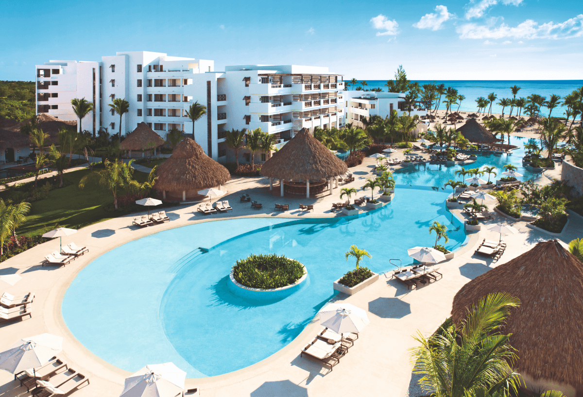Outdoor pool scene with loungers, parasols and bar at the Secrets Capa Cana Resort